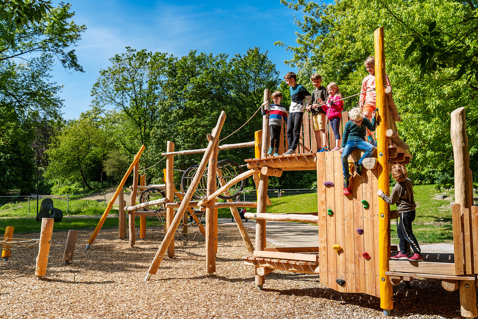 Kinder spielen auf einem Gerüst mit Kletterwand, Balancierelementen und Kletternetzen.